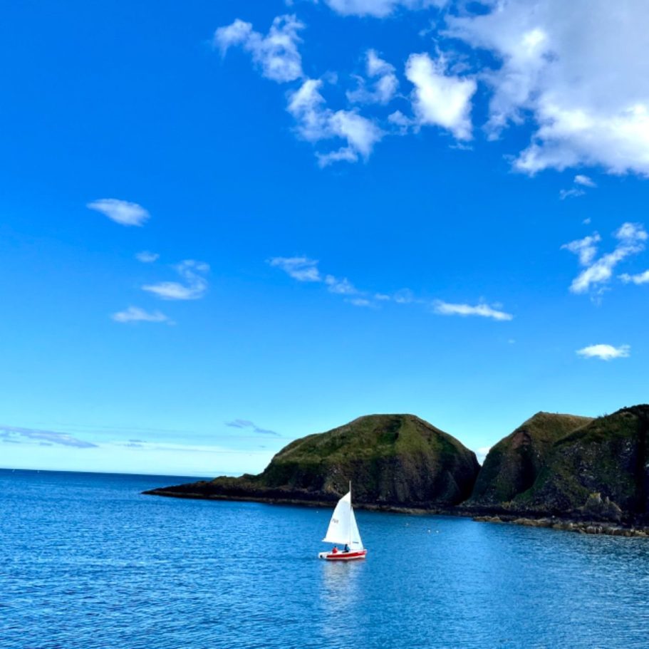 Segelboot auf ruhigem Meer vor grünen Klippen – Symbol für Weitblick, Klarheit und Kursbestimmung beim Go Beyond Retreat